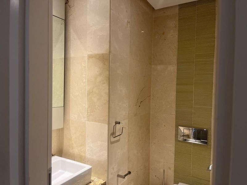 A compact bathroom featuring stone wall tiling, a wall-mounted toilet with a chrome flush plate, and a vessel sink on a stone vanity.