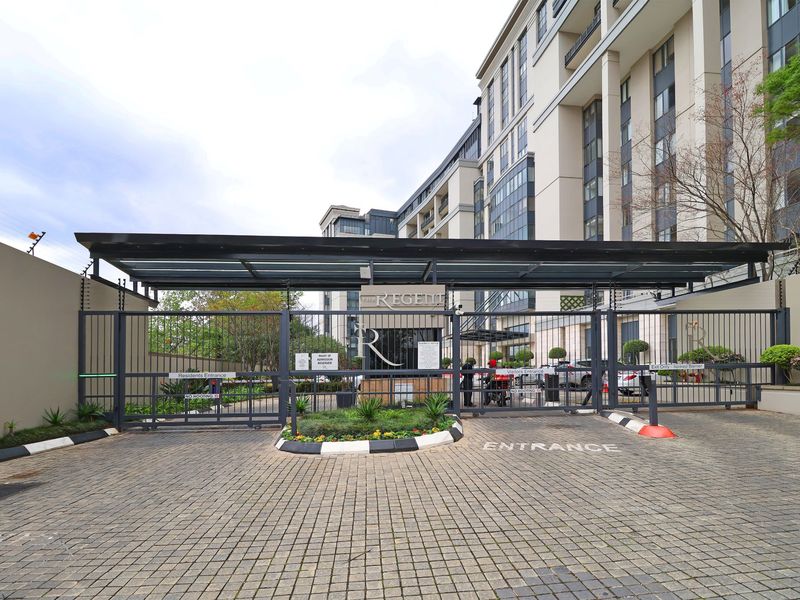The main entrance to the apartment complex features a secure gated access point with a paved driveway and a covered guard house.