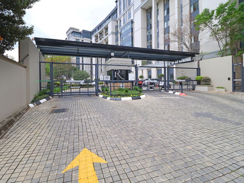 Secure gated entrance to the apartment complex featuring a guard house, paved driveway, and modern perimeter security infrastructure.