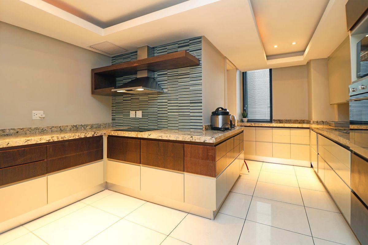Modern kitchen featuring granite countertops, high-end cabinetry, built-in oven, extractor fan, and stylish mosaic backsplash with recessed ceiling lighting.