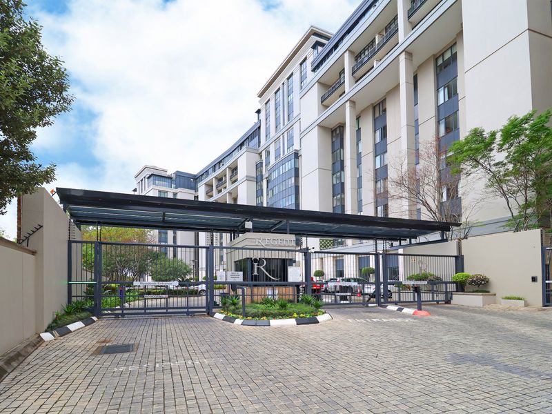 The main entrance to The Regent apartment complex, featuring a secure gated access point, guard house, and well-maintained paved driveway.