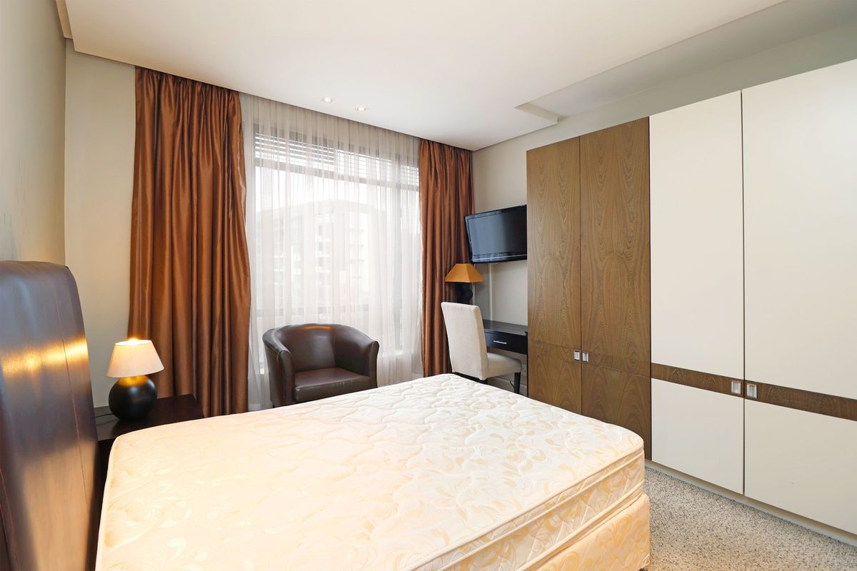 A well-maintained bedroom featuring built-in wardrobes with a mix of wood and white finishes, recessed ceiling lighting, and neutral carpeting.