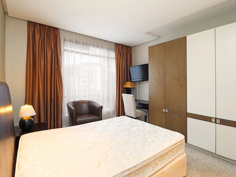 A well-maintained bedroom featuring built-in wardrobes with a mix of wood and white finishes, recessed ceiling lighting, and neutral carpeting.