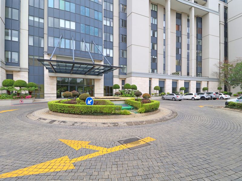The front entrance of the apartment complex features a paved circular driveway, landscaped roundabout, and a modern glass canopy over the main building entry.