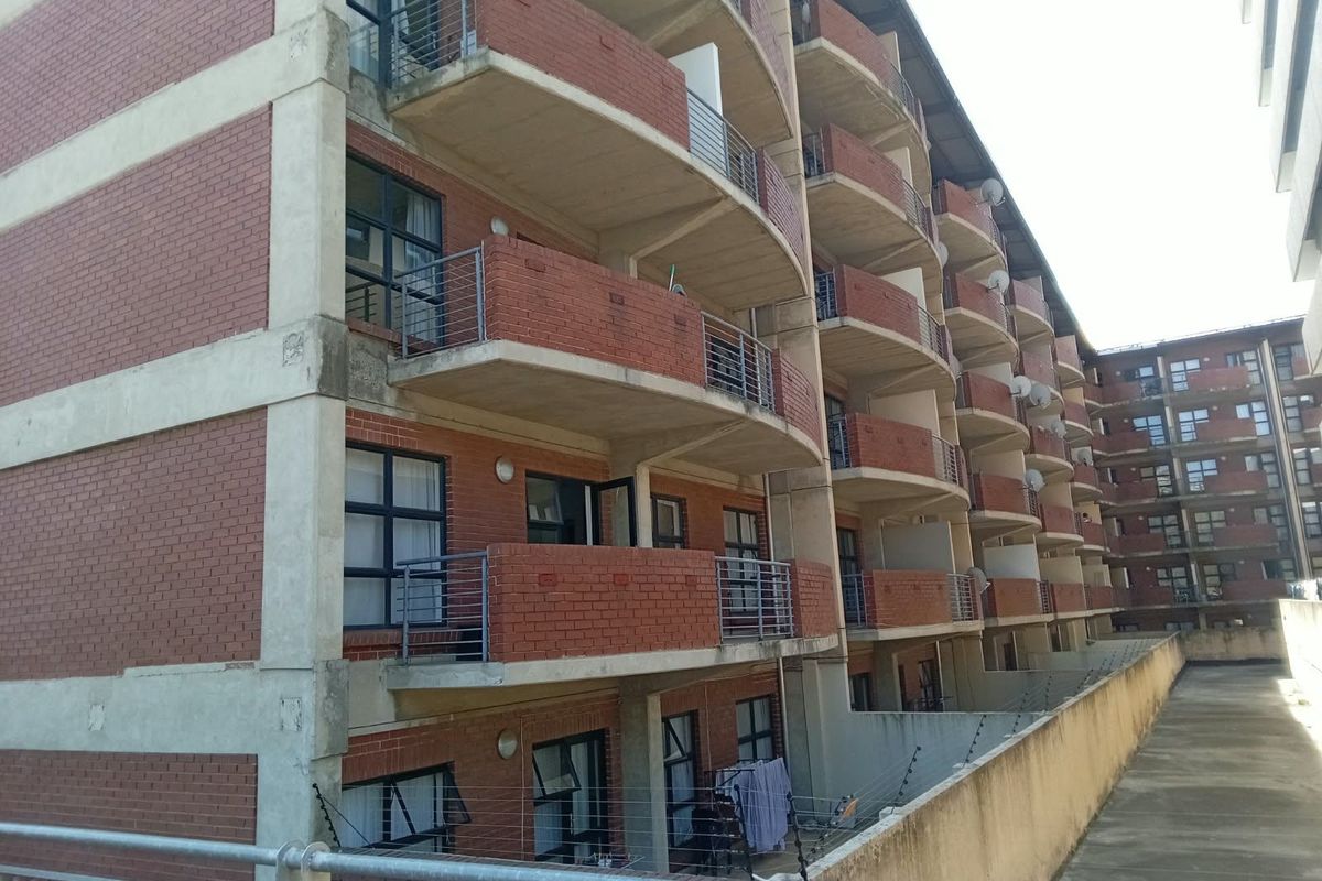 Exterior view of a multi-story townhouse complex featuring red brick facade, concrete balconies with metal railings, and perimeter electric fencing.
