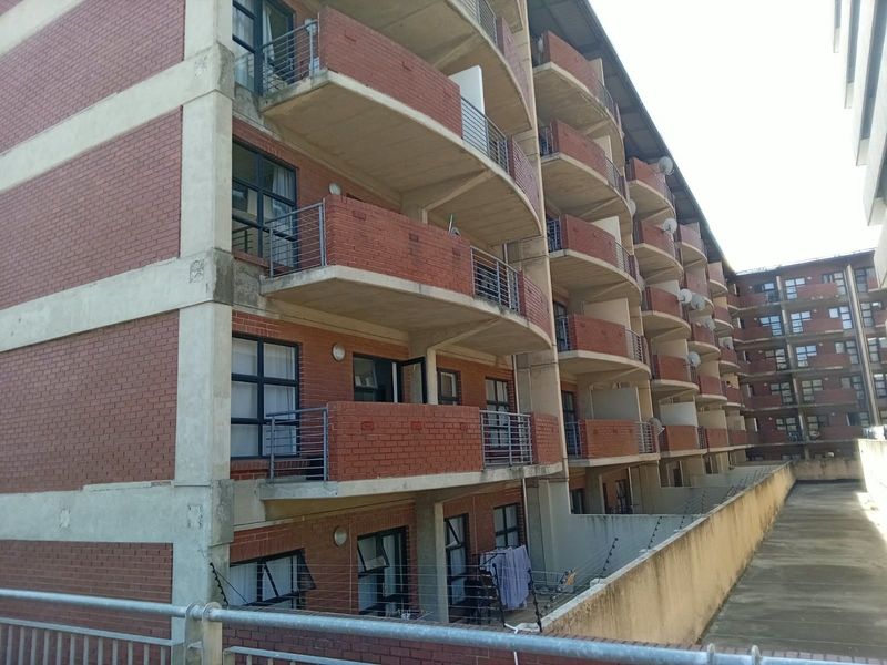 Exterior view of a multi-story townhouse complex featuring red brick facade, concrete balconies with metal railings, and perimeter electric fencing.