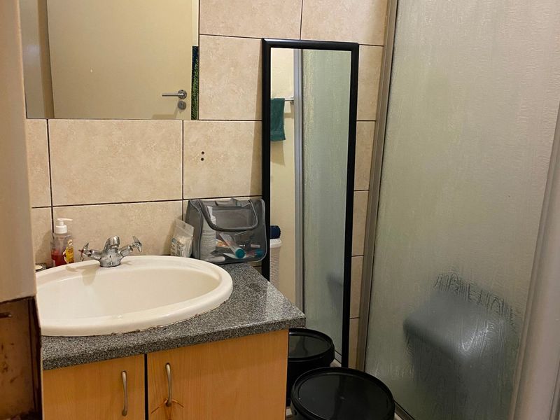 A functional bathroom featuring a vanity with granite countertop, wall-mounted mirror, and a glass-enclosed shower with neutral ceramic tiling.
