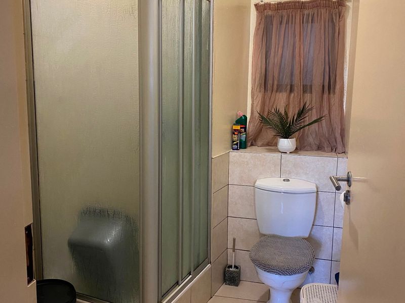 A functional bathroom featuring a corner shower enclosure, a standard toilet, tiled flooring, and an integrated extractor fan.
