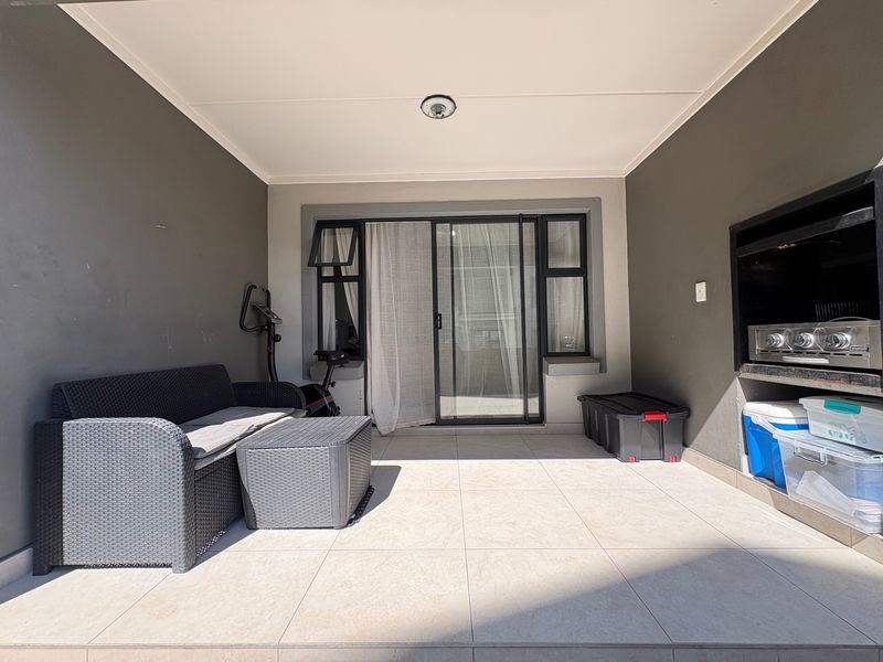 A covered patio featuring tiled flooring, a built-in braai, and sliding glass door access to the interior living space.