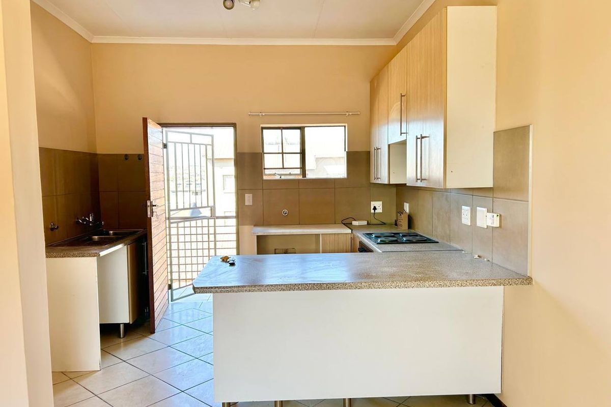 A functional kitchen featuring built-in cabinetry, a hob, and a double sink, with direct access to an exterior security gate.