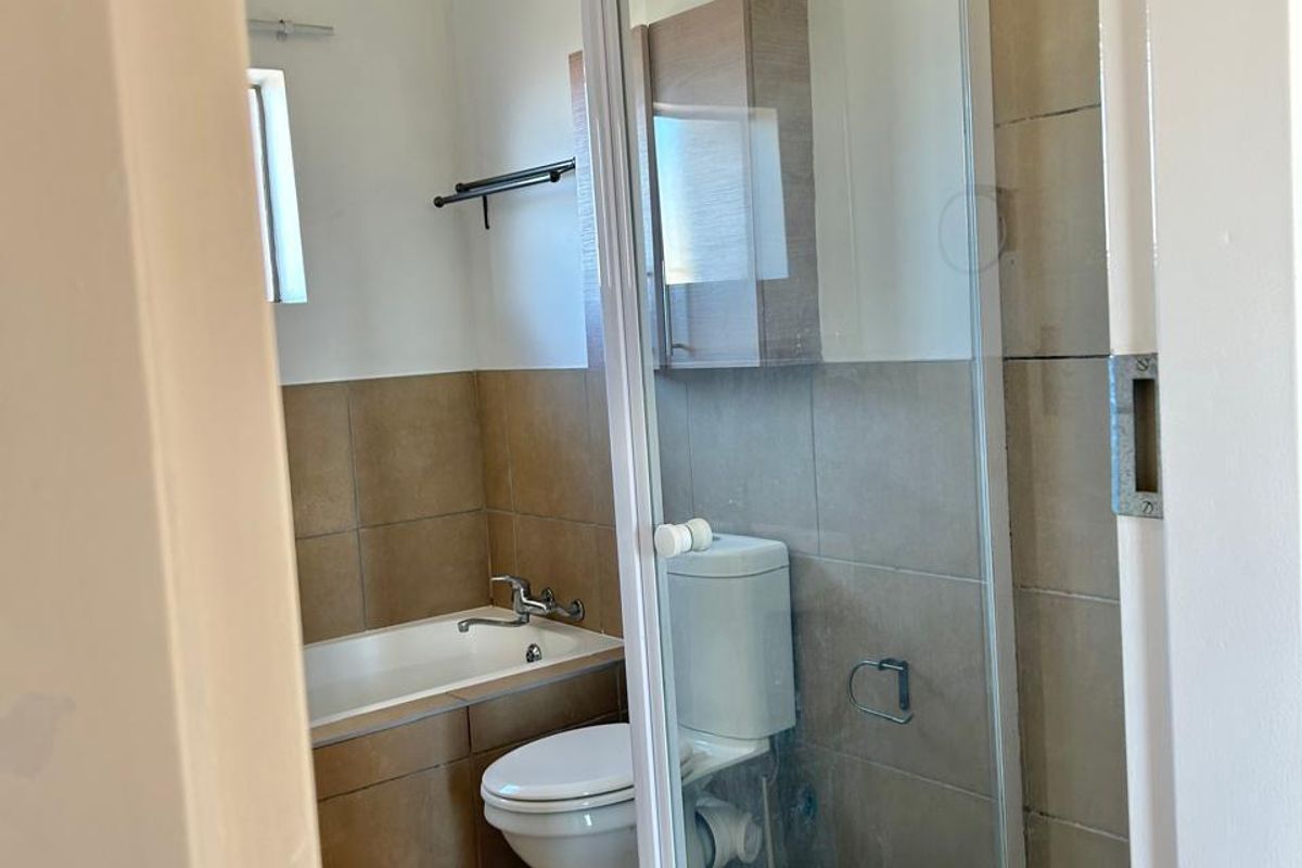 A functional bathroom featuring a bathtub, separate shower enclosure, toilet, and neutral wall and floor tiling.