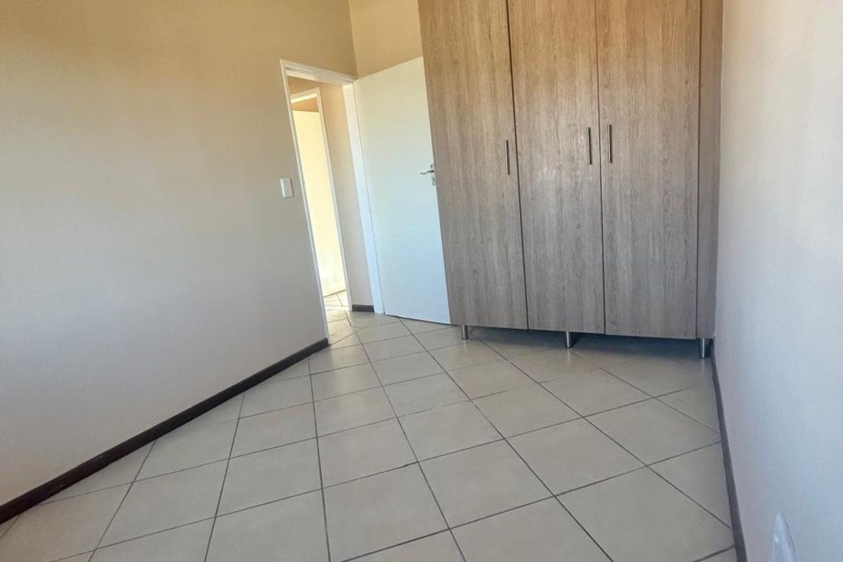 A clean, empty bedroom featuring neutral tiled flooring and a large, modern built-in wooden wardrobe.