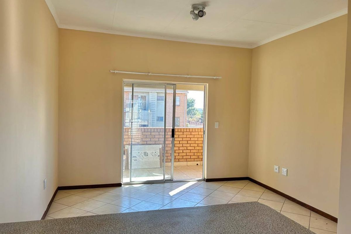 An empty living room featuring tiled flooring and a sliding glass door that opens onto a balcony.