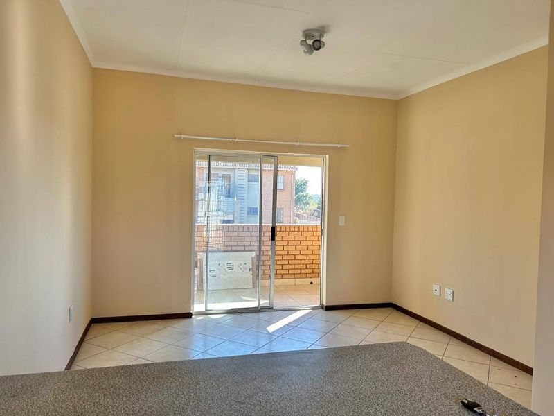 An empty living room featuring tiled flooring and a sliding glass door that opens onto a balcony.