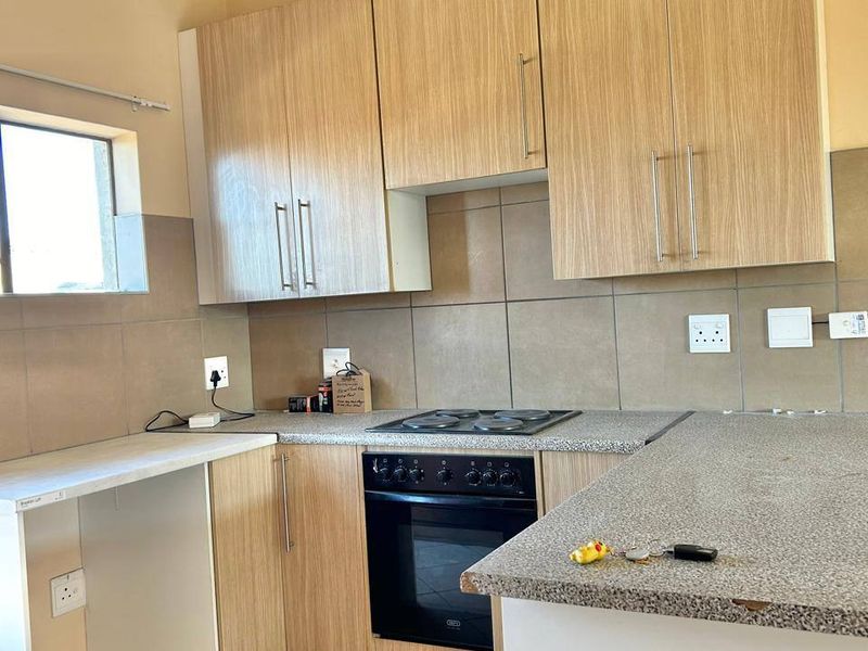 A functional kitchen featuring light wood-finish cabinetry, granite-look laminate countertops, a built-in electric oven and hob, and neutral tiled flooring.
