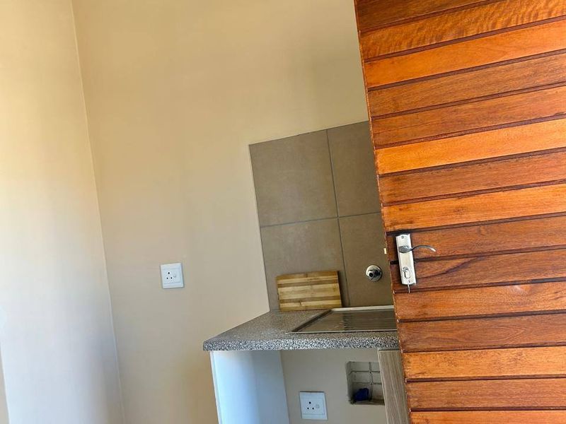 A compact kitchen area featuring a granite countertop, tiled backsplash, and a built-in hob, with a wooden door entrance.