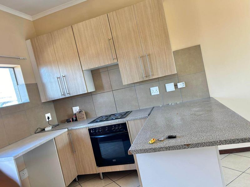 A functional kitchen featuring light wood-finish cabinetry, granite-look laminate countertops, a built-in oven with electric hob, and neutral tiled backsplash.
