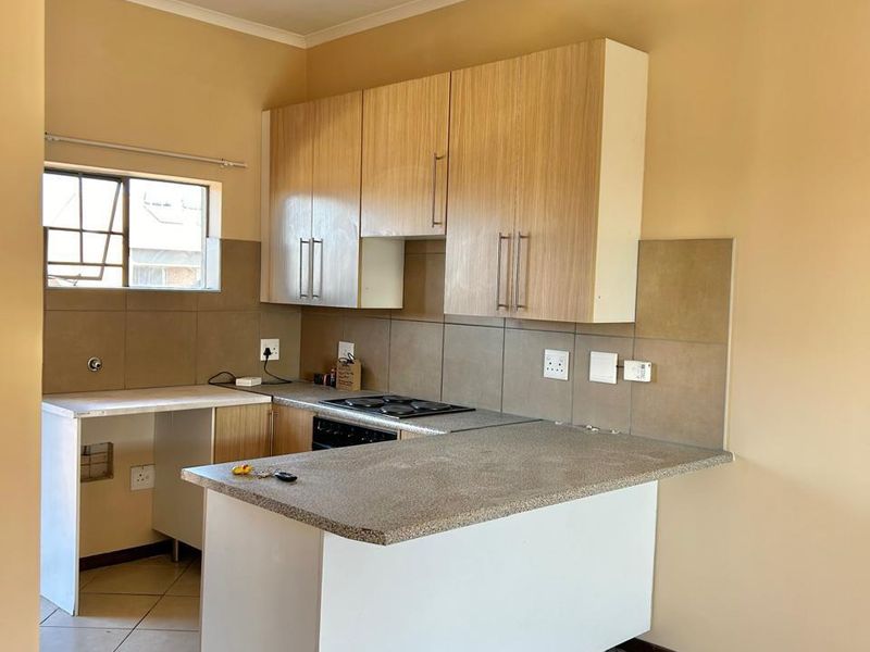 A functional kitchen featuring light wood-finish cabinetry, a built-in hob and oven, tiled backsplash, and a breakfast bar counter.