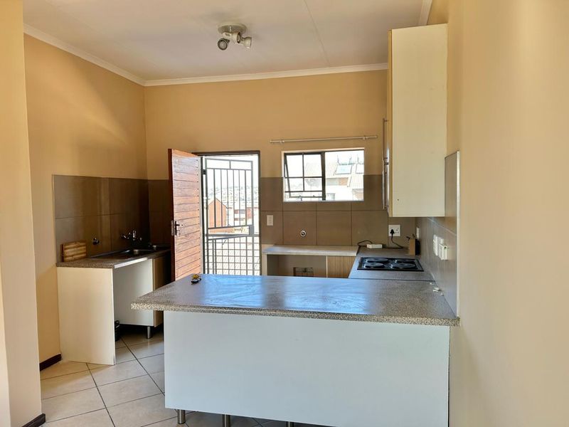 A functional kitchen featuring built-in cabinetry, a breakfast nook, electric hob, and tiled splashbacks, with direct access to an exterior security gate.