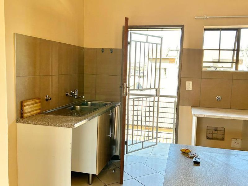 A functional kitchen area featuring tiled flooring, granite-look countertops, a double sink, and direct access to an exterior security gate.