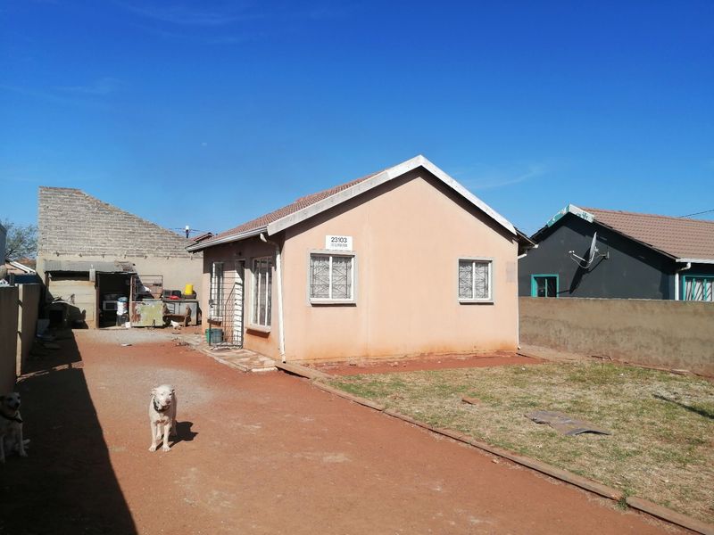Front view of a single-story residential house featuring a tiled roof, security bars on windows, and a surrounding perimeter wall with a driveway.