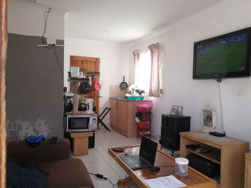 Open-plan living area featuring tiled flooring and a compact kitchen corner, showing signs of wall dampness and requiring maintenance.