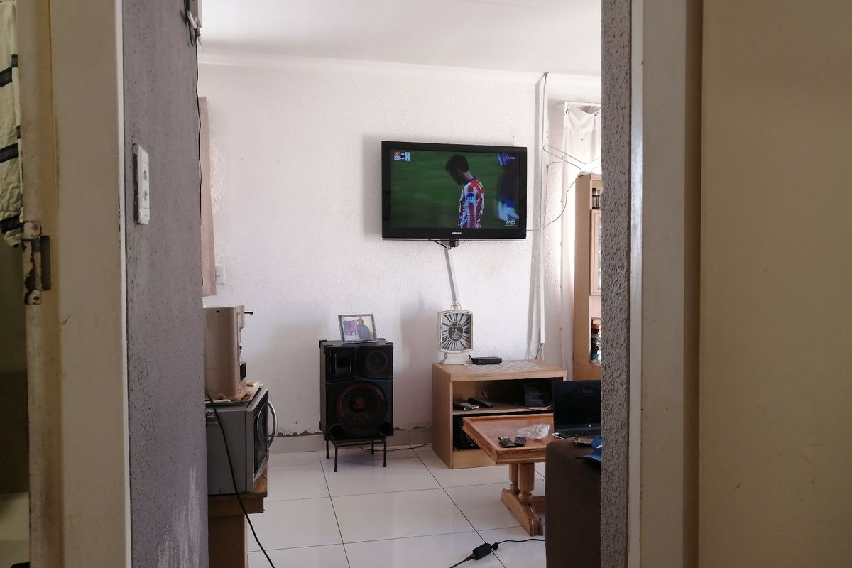 A living room area featuring tiled flooring and a wall-mounted television, viewed through a doorway.