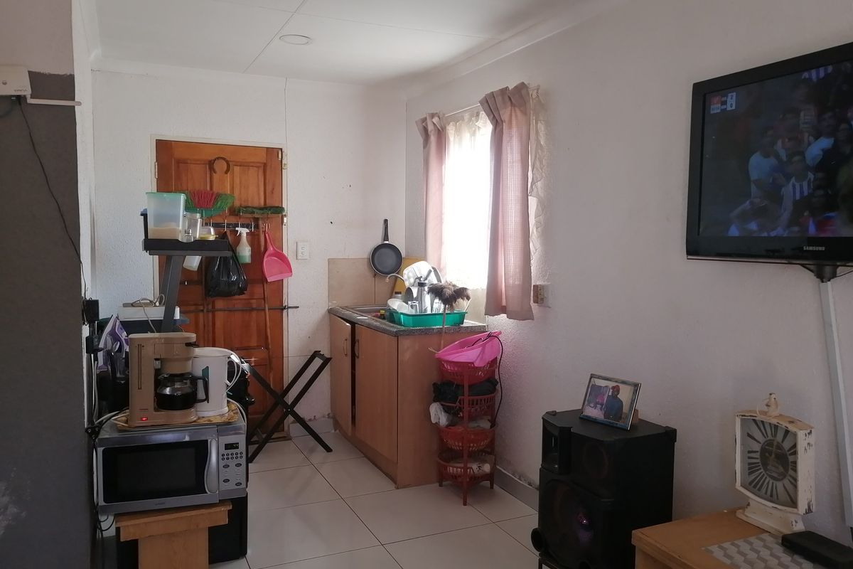 A compact kitchen area featuring basic cabinetry, a sink, and tiled flooring, requiring cosmetic updates to improve its overall condition and functionality.
