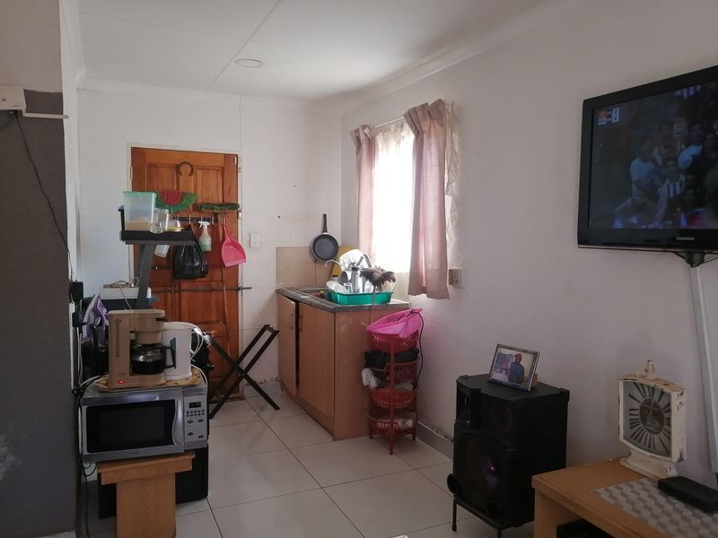 A compact kitchen area featuring basic cabinetry, a sink, and tiled flooring, requiring cosmetic updates to improve its overall condition and functionality.