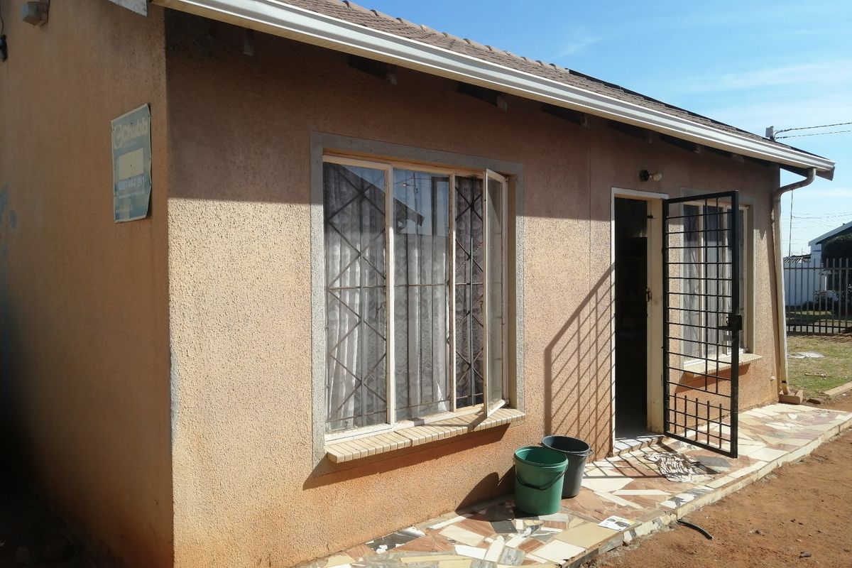 Rear exterior view of the house featuring a tiled patio area, security gate, and metal window frames with a textured wall finish.