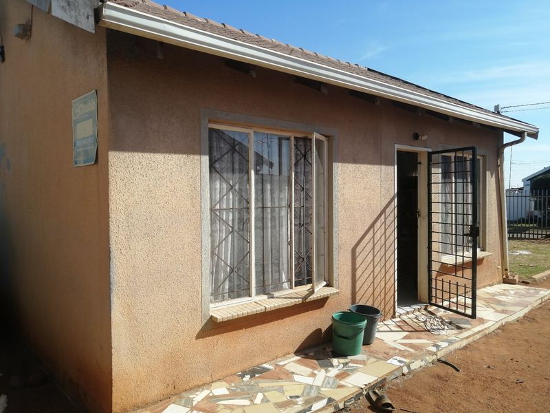 Rear exterior view of the house featuring a tiled patio area, security gate, and metal window frames with a textured wall finish.