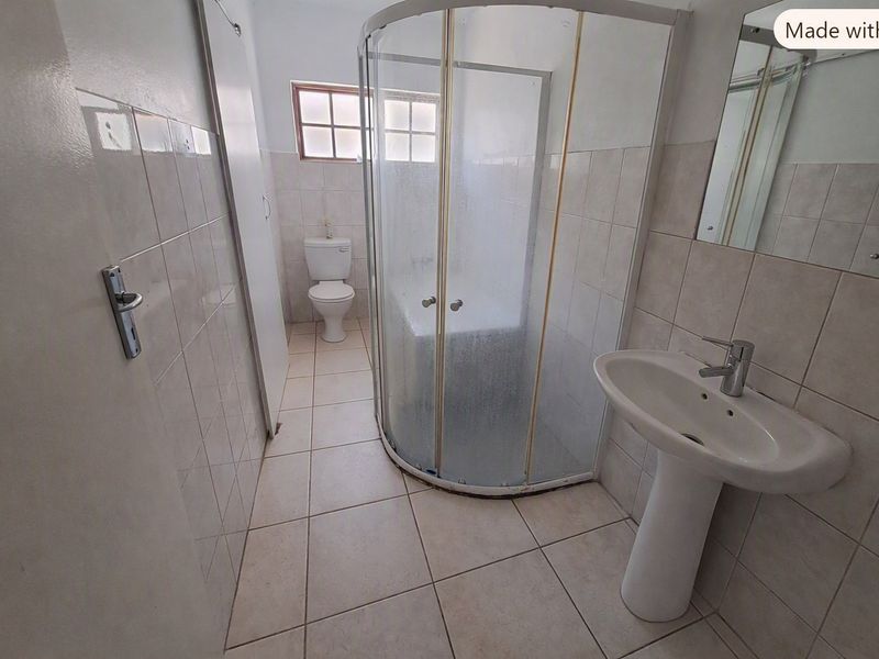A functional bathroom featuring a pedestal basin, a corner shower enclosure, and a toilet with neutral wall and floor tiling.