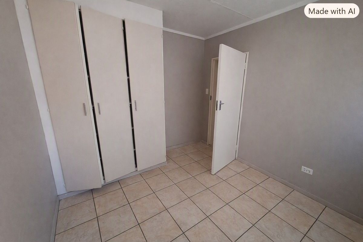 A clean, empty bedroom featuring neutral grey walls, tiled flooring, and built-in cupboards, offering a versatile space ready for personalization.
