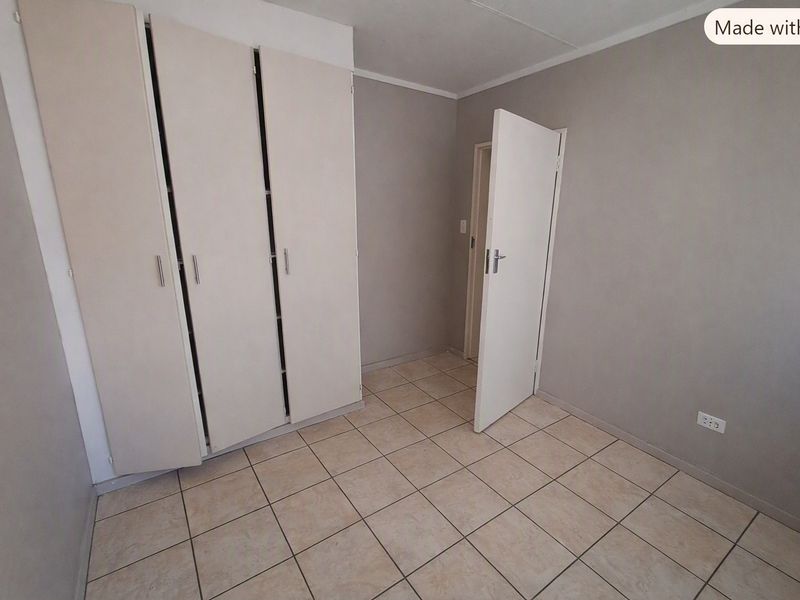 A clean, empty bedroom featuring neutral grey walls, tiled flooring, and built-in cupboards, offering a versatile space ready for personalization.