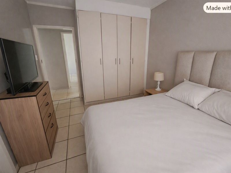 A functional bedroom featuring built-in cupboards and neutral tiled flooring, providing a clean and practical living space.