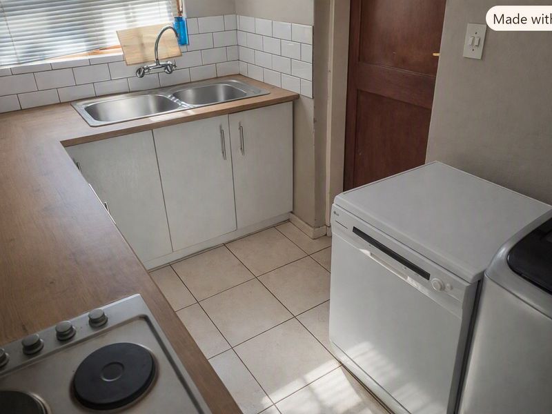 A functional kitchen featuring a double bowl sink, subway tile backsplash, laminate countertops, and a built-in hob with tiled flooring.