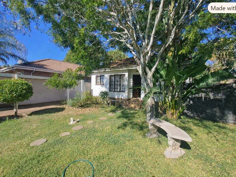 A view of the rear garden and building exterior featuring a lawn, mature trees, and a paved pathway leading to the house entrance.