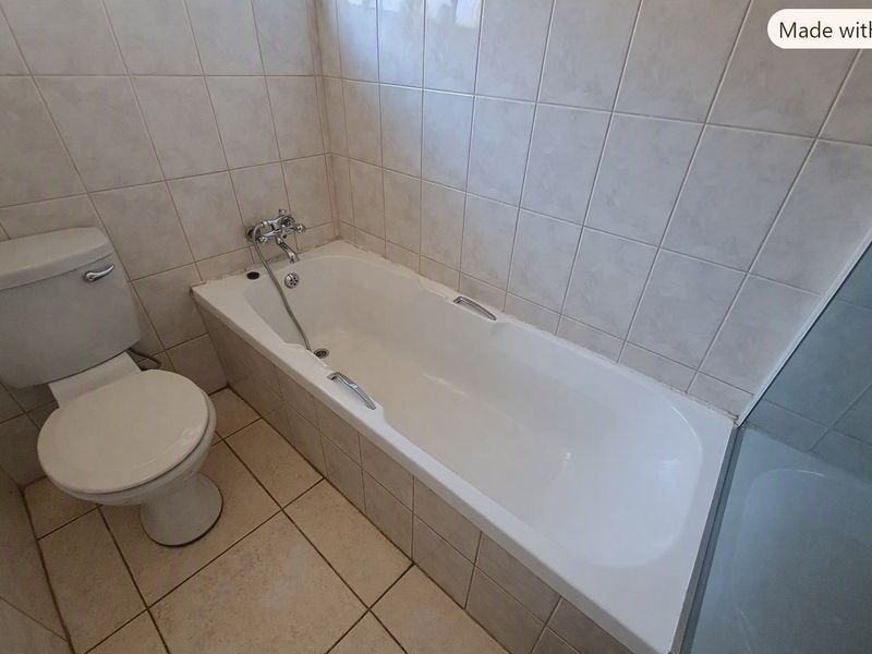A functional bathroom featuring a standard bathtub, toilet, and neutral wall and floor tiling.