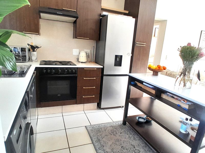 A functional kitchen featuring dark wood cabinetry, built-in oven and hob, extractor fan, and tiled flooring with a central island unit.
