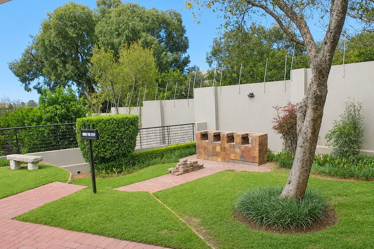 A well-maintained rear garden featuring a paved walkway, established tree, and a built-in brick braai area enclosed by a secure perimeter wall.