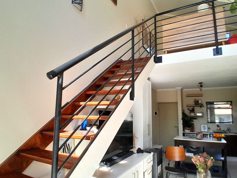 Open plan living area featuring a wooden staircase leading to a mezzanine level, tiled flooring, and integrated cabinetry.