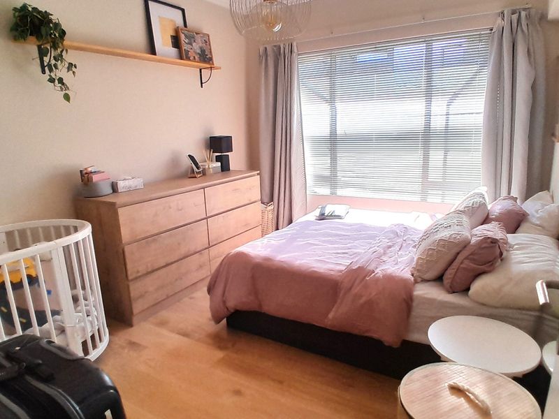 A well-lit bedroom featuring laminate flooring, a large window with venetian blinds, and a floating wall shelf.