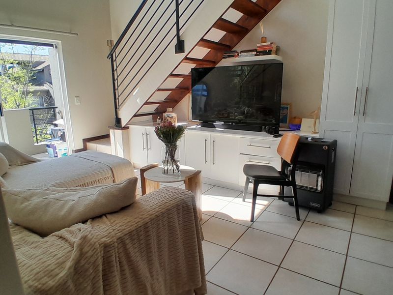 A bright living room featuring tiled floors, built-in storage cabinetry, and an open staircase leading to an upper level with balcony access.