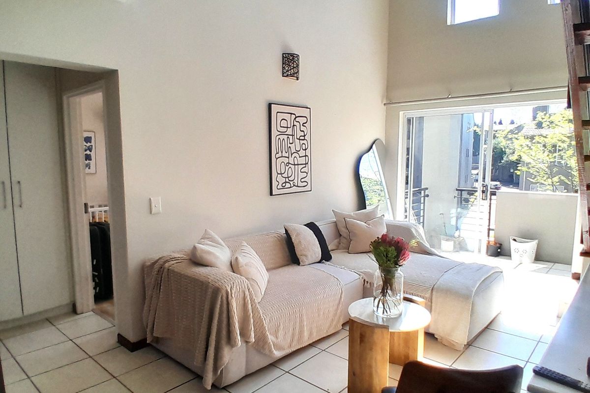 Bright living room featuring double volume ceilings, tiled flooring, and large sliding glass doors leading to a private balcony.