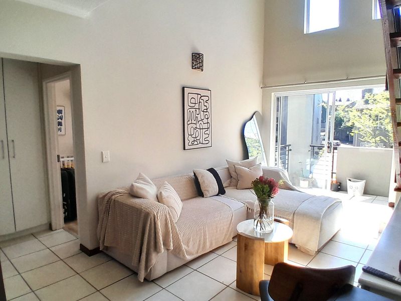 Bright living room featuring double volume ceilings, tiled flooring, and large sliding glass doors leading to a private balcony.