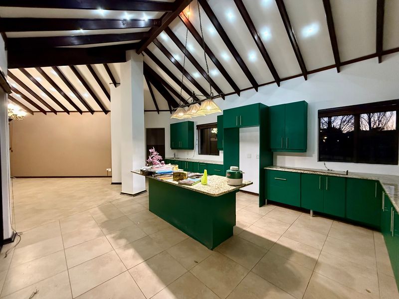 Spacious open-plan kitchen and living area featuring high vaulted ceilings with exposed timber beams, granite countertops, and modern green cabinetry.