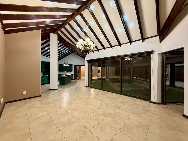 Spacious open-plan living area featuring high vaulted ceilings with exposed timber beams, tiled flooring, and large sliding doors overlooking the pool area.