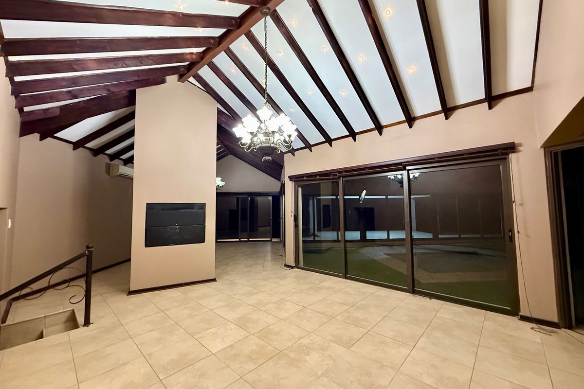 Spacious living area featuring high vaulted ceilings with exposed timber beams, tiled flooring, a built-in fireplace, and large sliding glass doors leading outdoors.