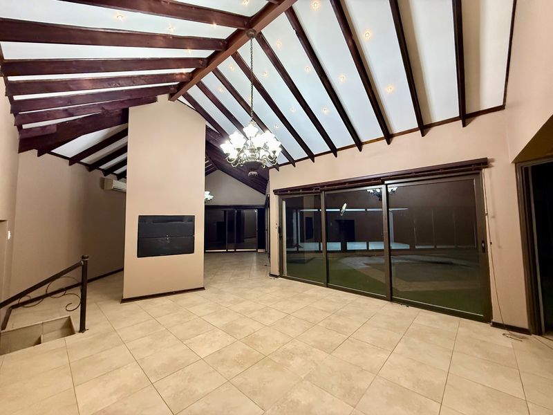 Spacious living area featuring high vaulted ceilings with exposed timber beams, tiled flooring, a built-in fireplace, and large sliding glass doors leading outdoors.