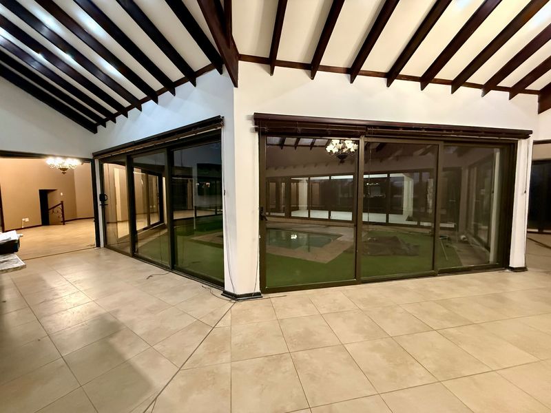 Spacious living area featuring high vaulted ceilings with exposed timber beams, neutral tiled flooring, and large sliding glass doors overlooking the pool area.